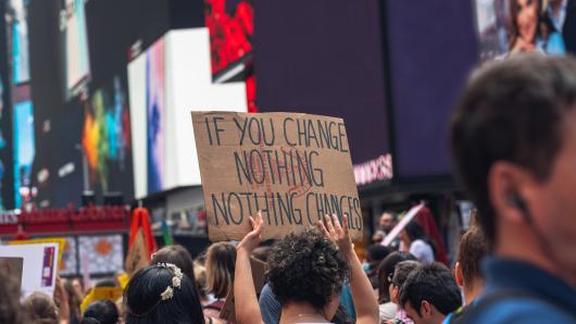 Someone holds up a poster that reads "if you change nothing, nothing will change" during a protest in a city.