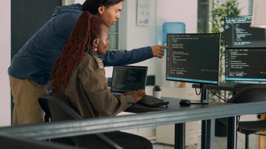 Two people looking at code on a computer screen.