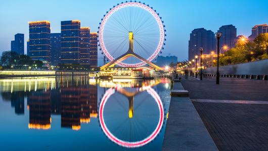 an image of a ferris wheel framed against a city and with reflecting water in the foreground