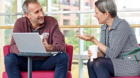 A male and a female executive talk sitting down with an open laptop
