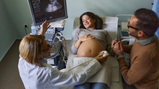 A sonogram technician performs an ultrasound on a pregnant person.