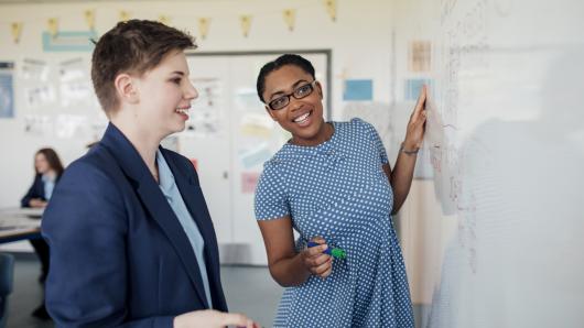 Side view of teenage student getting her work on whiteboard checked by the teacher.