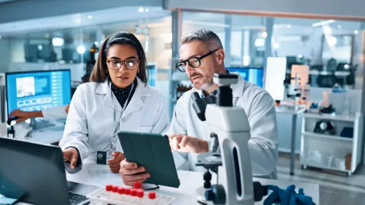Two health care workers in a lab looking at a tablet