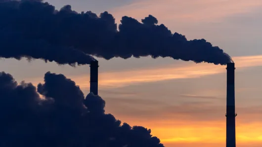 Smoke stack emitting black smoke against the sunset