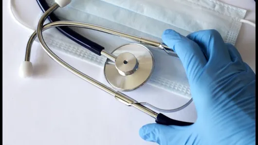 blue-gloved hand reaching for stethoscope on table on top of medical mask.