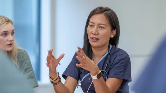 A woman in scrubs speaks to a group of colleagues.