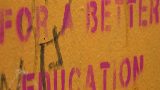 Orange wall with pink block letters that say For a Better Education