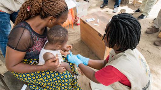 Health worker administering a shot to a child being held by the mother