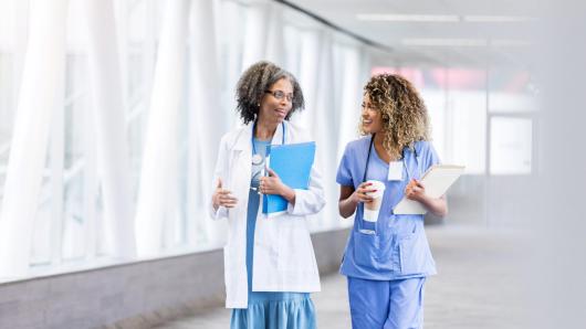 Two health care workers conversing while walking down a hallway