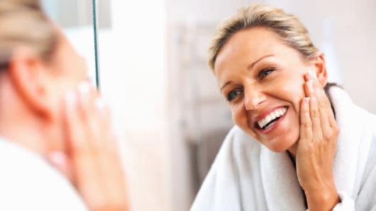 A woman smiling and looking into a mirror.