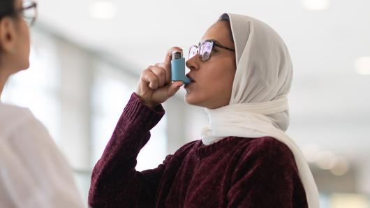 A Muslim woman tests her puffer for her asthma treatment with doctor watching. 