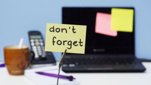 Post it note with words don't forget written on it in front of lap top and phone