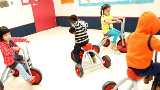 Four kids on trikes riding around the classroom.