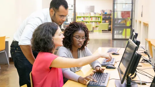 Three people in library reviewing on computer.
