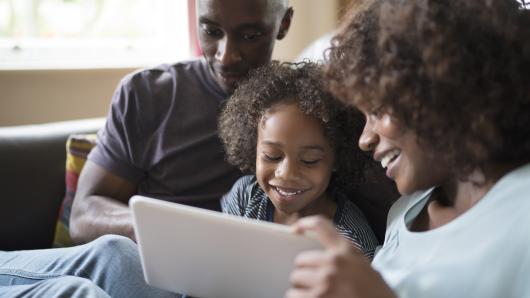 Two adults and child smiling on couch looking at tablet