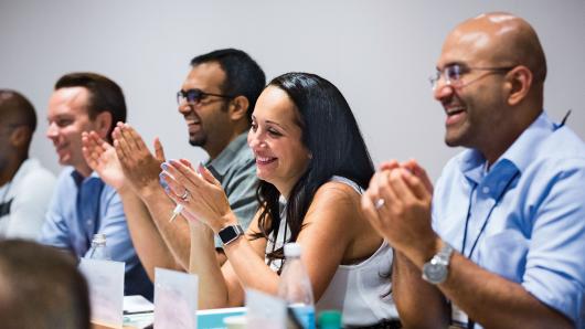 A diverse group of four executives clapping in a HBS classroom