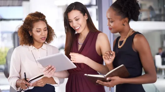 Three black female executives looking at a tablet