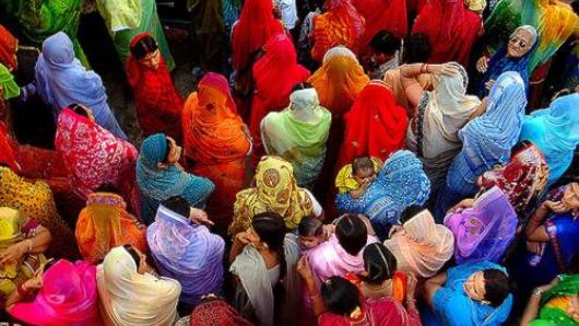 group of people with backs to camera, likely women but some heads are covered, in bright colorful garb