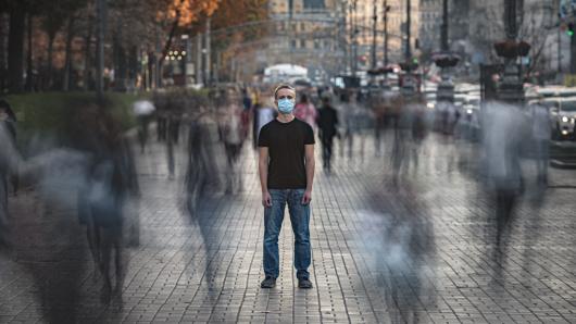 Masked person standing alone in a moving crowd